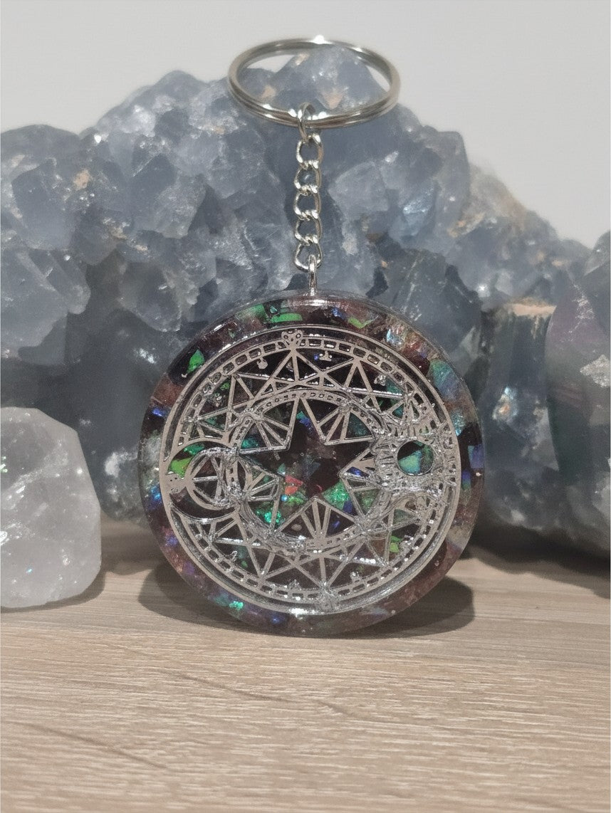 Pendentif orgonite AlyJoyCreation rond avec symbole céleste argenté et éclats irisés sur fond de cristal bleu