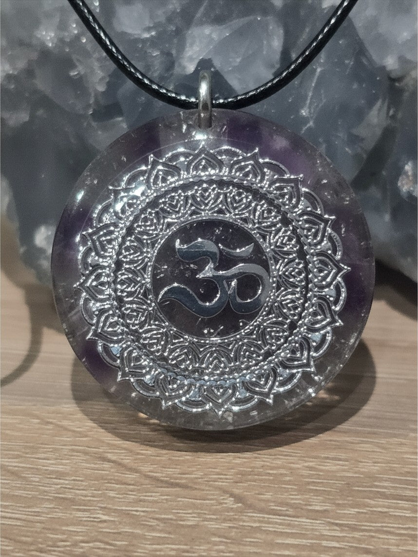 Pendentif Orgonite OM AlyJoyCreation rond avec symbole argenté sur fond violet, idéal pour équilibrer votre énergie.