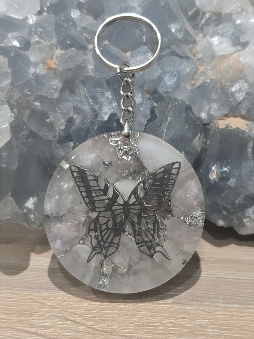 Pendentif orgonite AlyJoyCreation rond et transparent avec un motif papillon en métal sur fond de cristal bleu